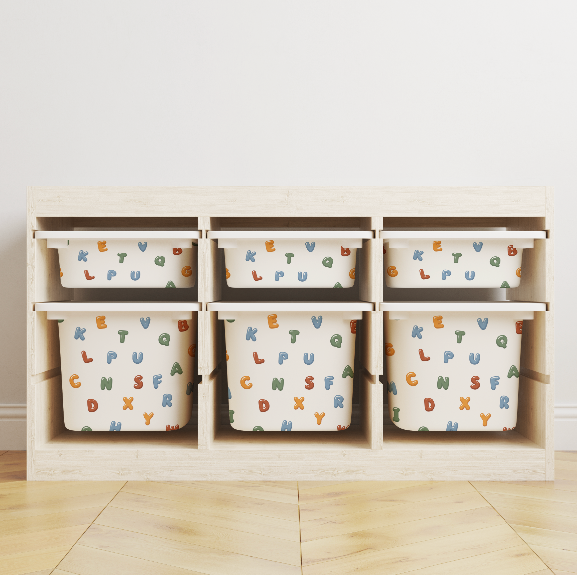 A IKES TRofast storage organiser with six cubby bins, each containing a white fabric storage bag printed with colourful alphabet letters, set against a plain white wall and light wood floor.
