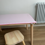 Wooden table with a pink checkered tablecloth and matching stool in a room with a radiator.