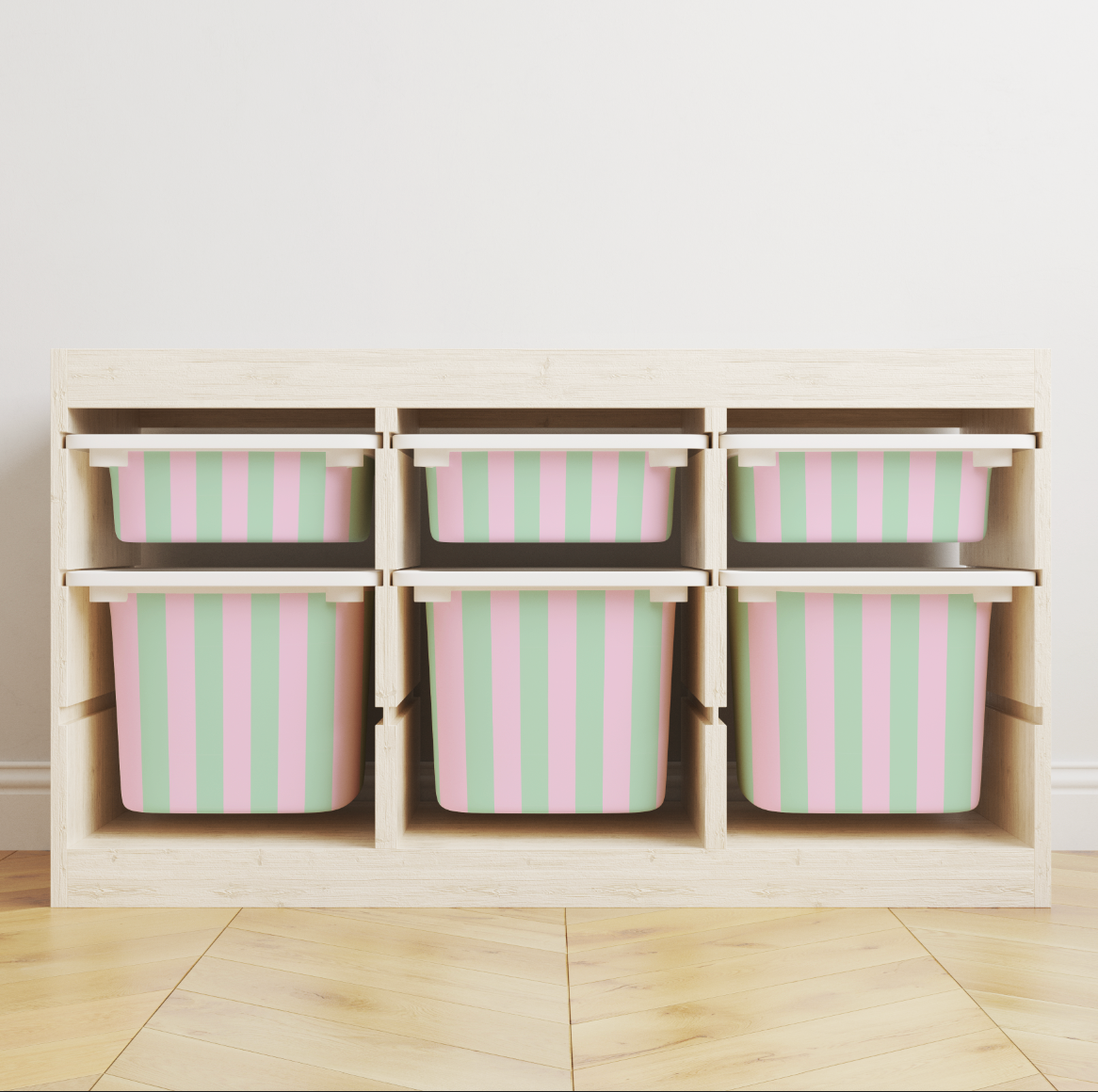 A light wood storage organizer with six cubby bins, each containing a pink and mint green striped plastic storage container, set against a neutral wall and light wood floor.