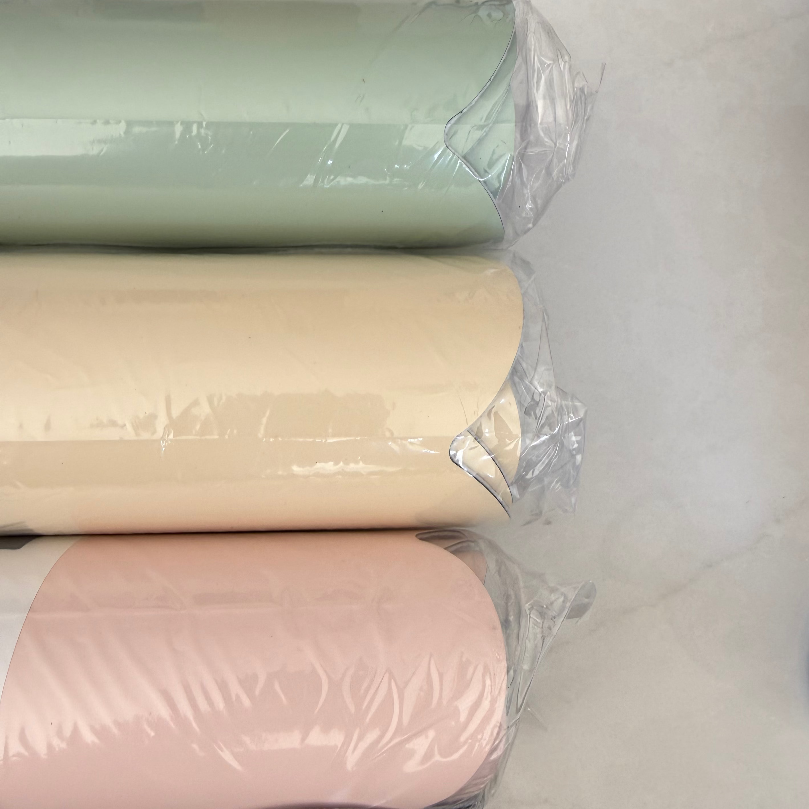 Three rolls of pastel-colored paper wrapped in plastic on a white surface.